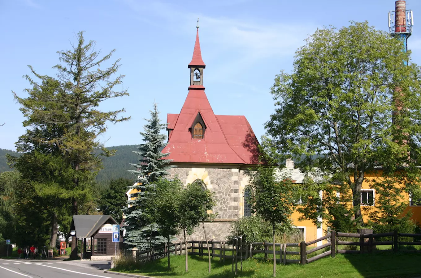 Kostel v Harrachově s červenou střechou mezi stromy.