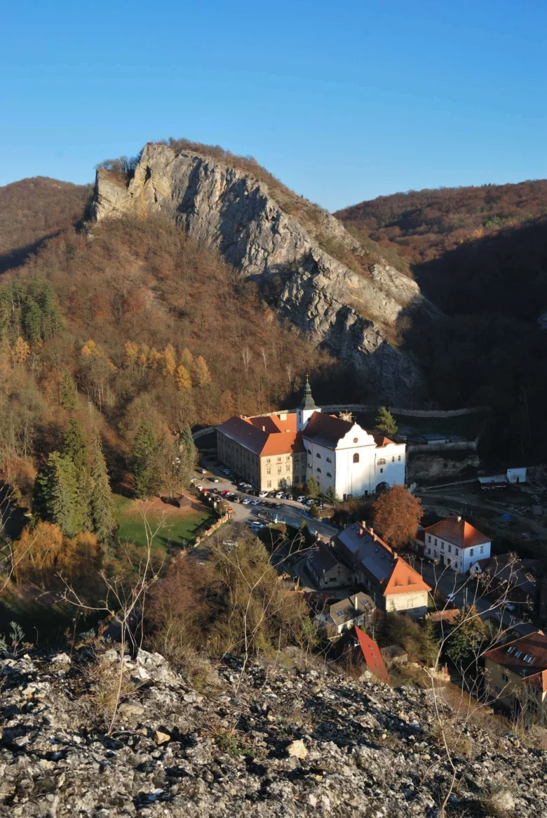 Pohled na klášter v údolí s lesy pod modrou oblohou.