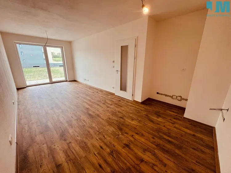 Prázdný byt s dřevěnou podlahou a velkými okny v Jihlavě.