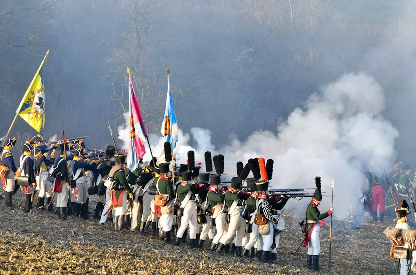 Rekonstrukce bitvy u Slavkova s vojáky v historických uniformách střílejícími z pušek.