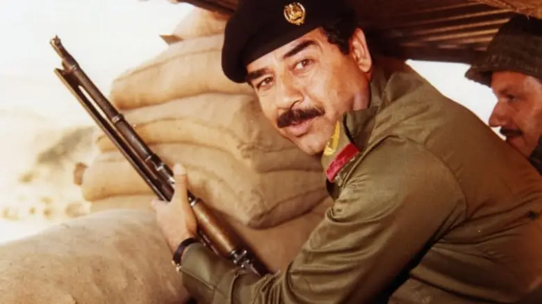 Saddam Husajn v vojenské formě s puškou za pytlů.