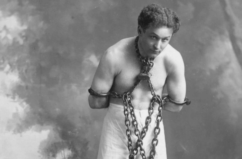 Harry Houdini vázaný řetězy v historické fotografii.