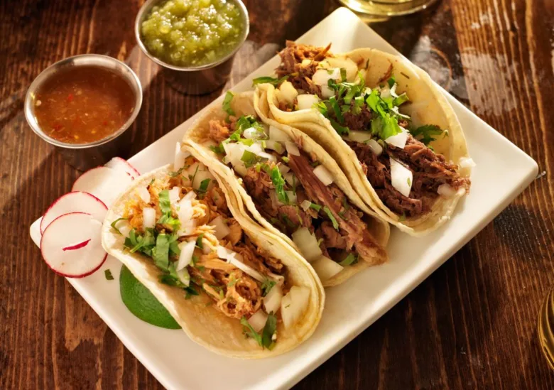 Tři mexické tacos s mletým masem a zeleninovými přílohami.