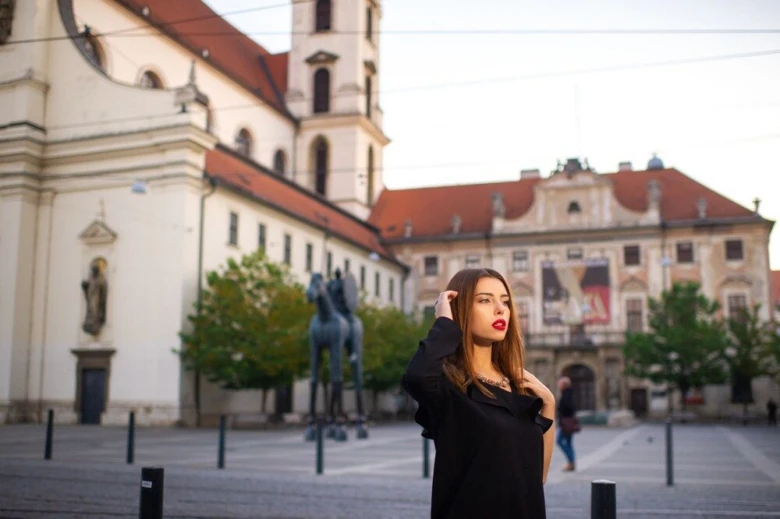 Žena stojí na brněnském náměstí s historickými budovami v pozadí.
