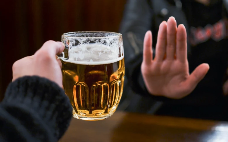 Ruka drží pivo s gestem odmítnutí pití alkoholu.