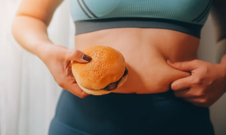 Žena drží burger a táhne si tuk na břiše.