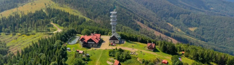 Vzdušný pohled na stanici s věží v horách a okolním lesu.