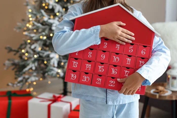 Dítě drží červený adventní kalendář v podobě domečku.