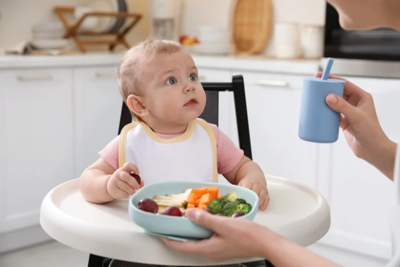 Malé dítě v jídelní židli s misky zeleninového pyré.