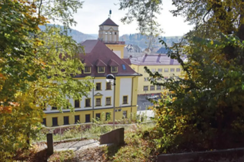 Žlutá budova v Kráslicích obklopena podzimními stromy.
