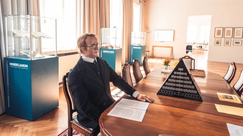 Gregor Mendel sedí u stolu s pyramidou genetiky v muzeu.