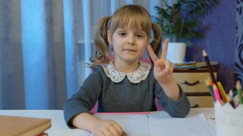 Malá dívka sedí u stolu a ukazuje prstík.
