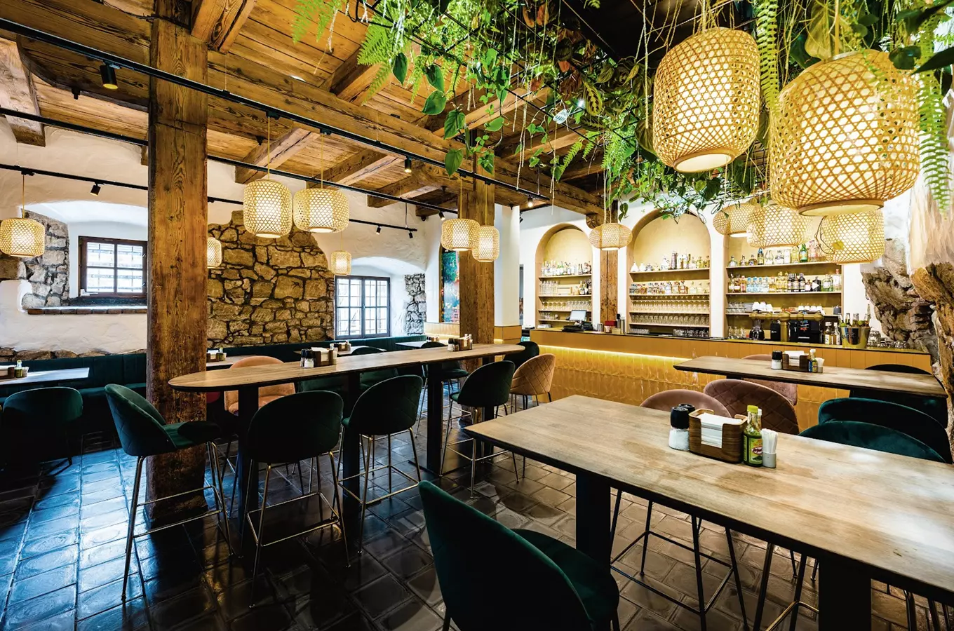 Interiér restaurace s dřevěnými sloupy, rostlinami na stropě a svítidly.