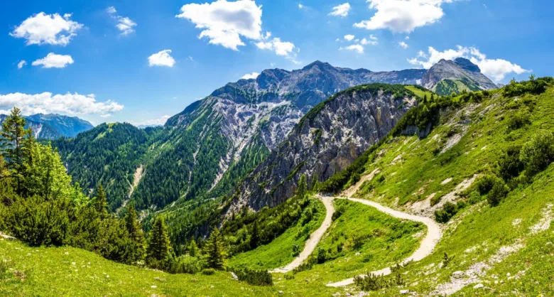 Zelené svahy Rakouských Alp s turistickou stezkou vedoucí k horám.