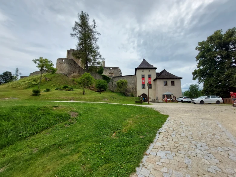 Zámek na kopci s trávníkem a kamennou cestou pod mraky.