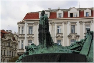Socha Jana Husa na pražském náměstí s historickými budovami v pozadí.