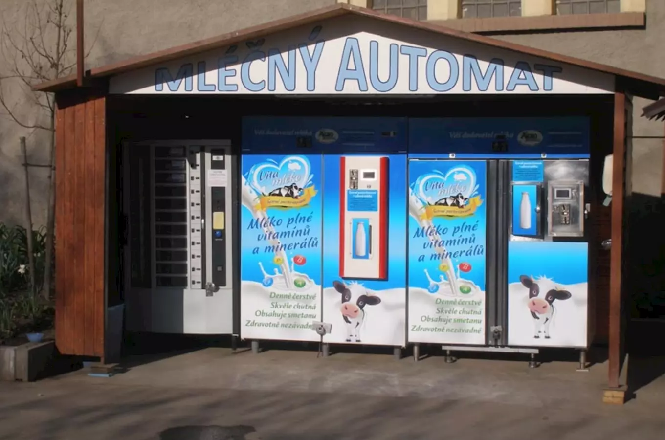 Venkovní mlékomat s reklamou na vitamínové mléko pod štítem MLÉČNÝ AUTOMAT.
