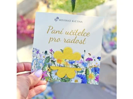 Ruka drží květinovou pohlednicu s textem Paní učitelce pro radost.