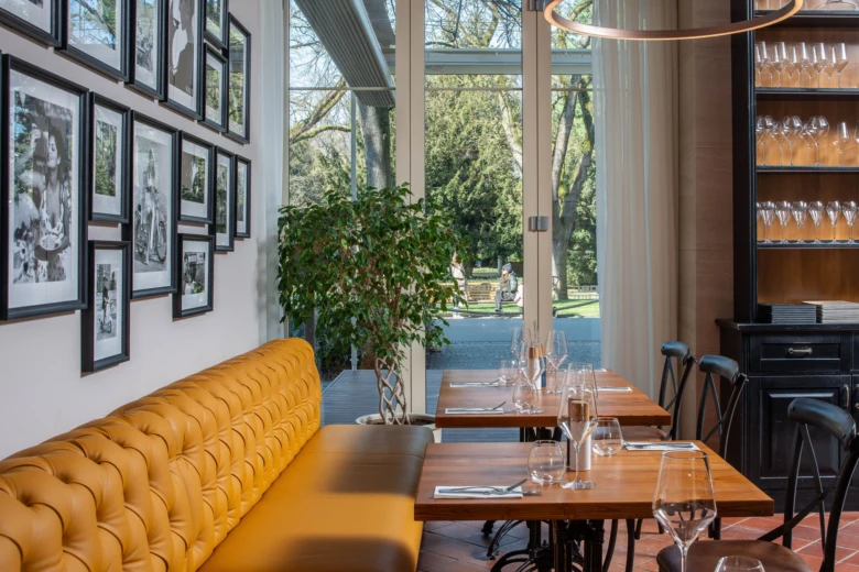 Interiér restaurace s žlutými lavicemi a okny do zahrady.