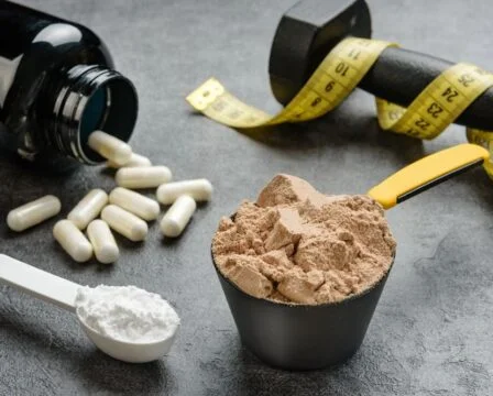 Proteiny, kapsle, činka a pásková míra pro kondici.