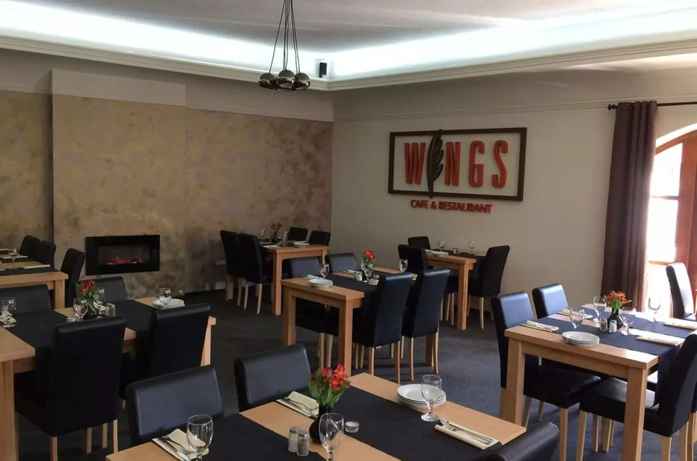 Interiér restaurace s dřevěnými stoly, židlemi a krbem.