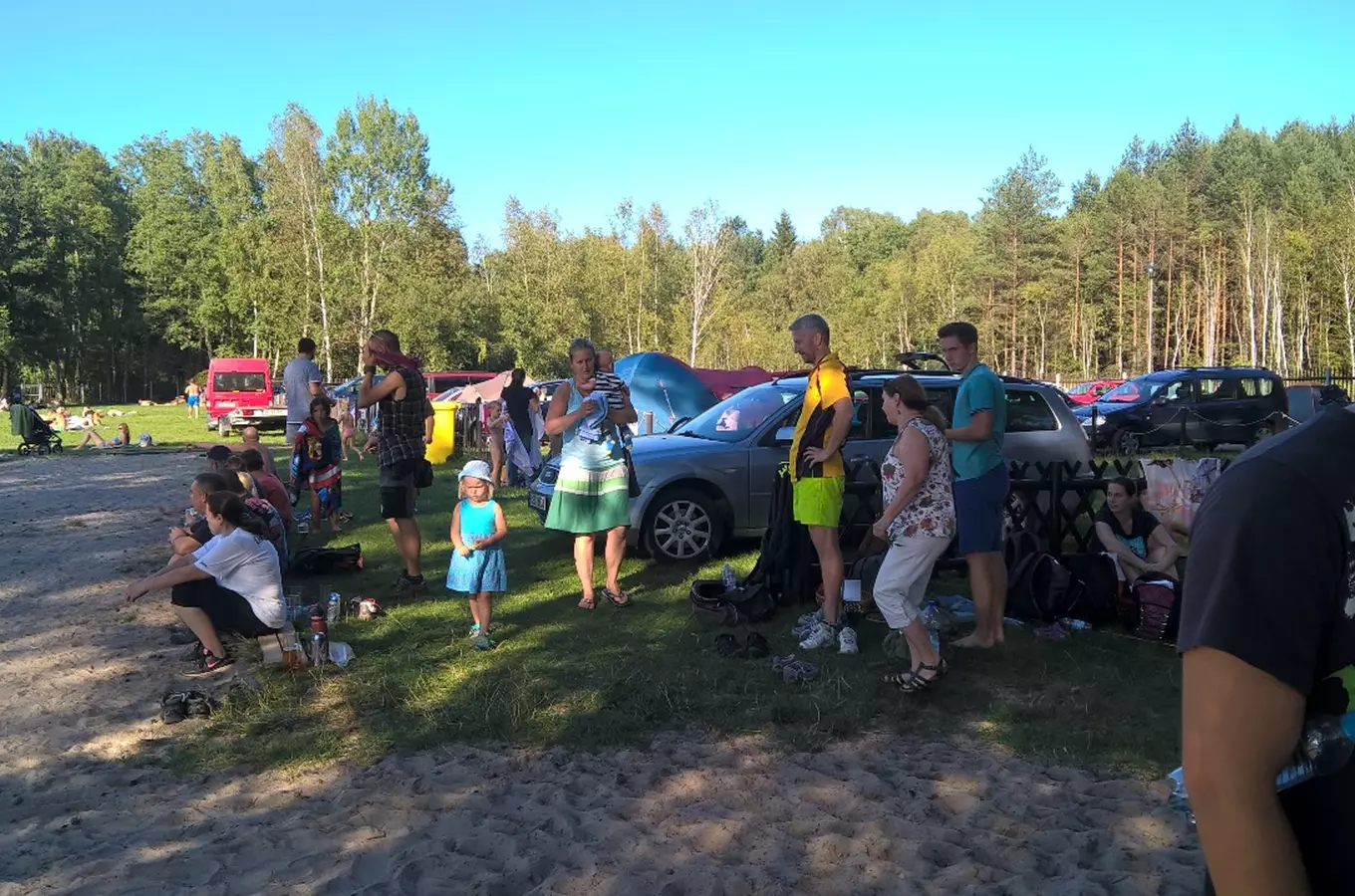 Lidé kempují u aut a stanu na slunečním místě.