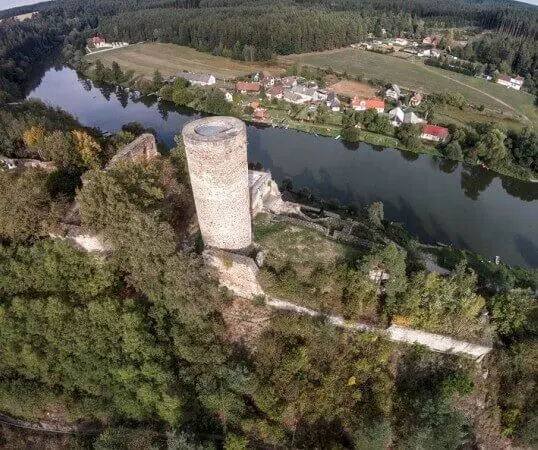 Zřícenina hradu v Bečyni nad řekou s okolní vesnicí.