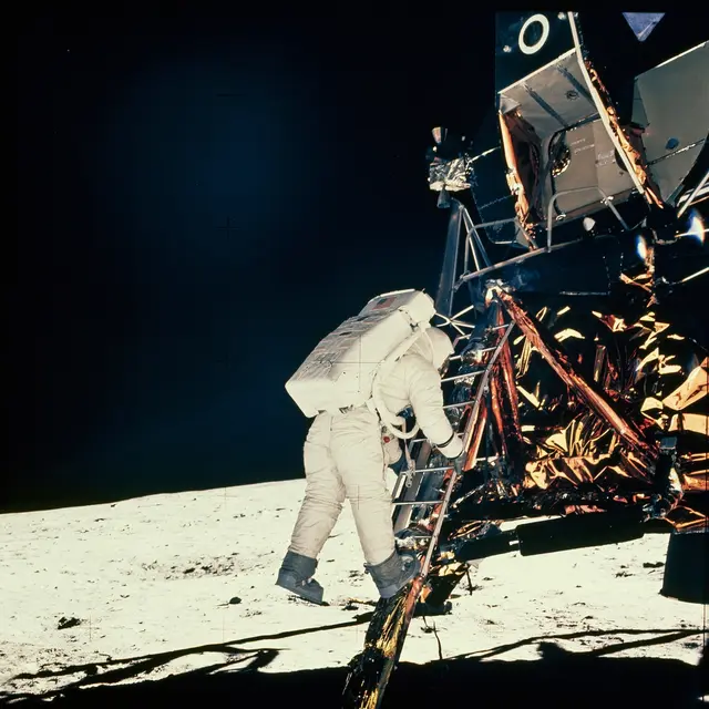 Astronaut sestupuje po žebříku lunárního modulu na povrchu Měsíce.