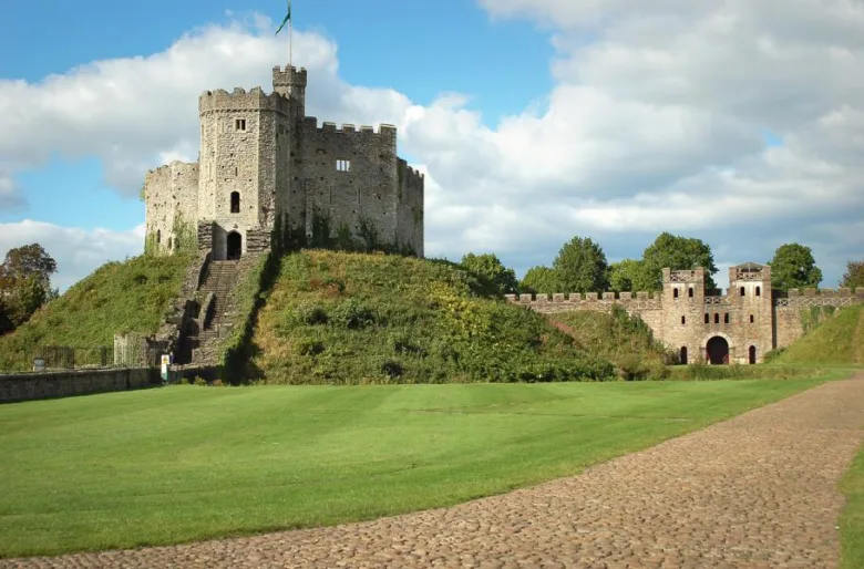 Zámek Caerphilly ve Walesu na trávnaté vyvýšenině pod modrou oblohou.