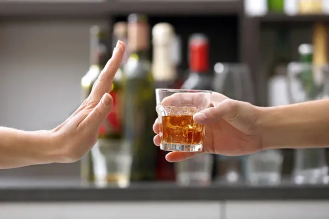 Ruka odmítá skleničku s alkoholem před barem.