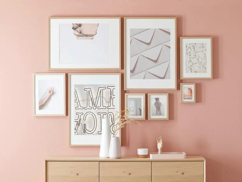 Moderní galerie s rámy na růžové stěně nad dřevěnou skříňkou.