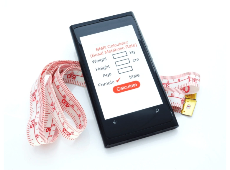 Smartfon s kalkulačkou BMR vedle měřicí pásky pro hubnutí.