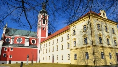 Kostel sv. Václava v Pačově s žlutým klášterním domem.
