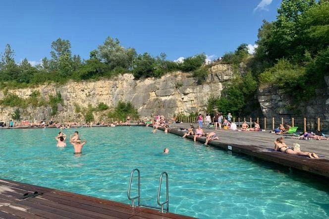 Přírodní koupaliště v lomu s lidmi ve vodě na slunci.