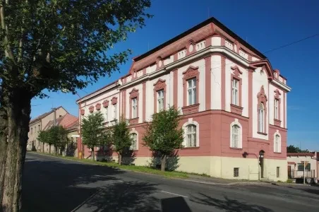 Historická budova v Hlinsku s růžovými fasádami a zelenou zeleň.
