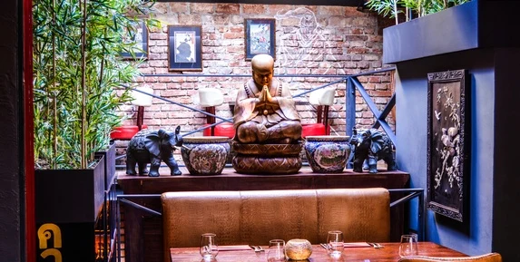 Interiér asijské restaurace s Buddhou, slony a cihlovou zdí.