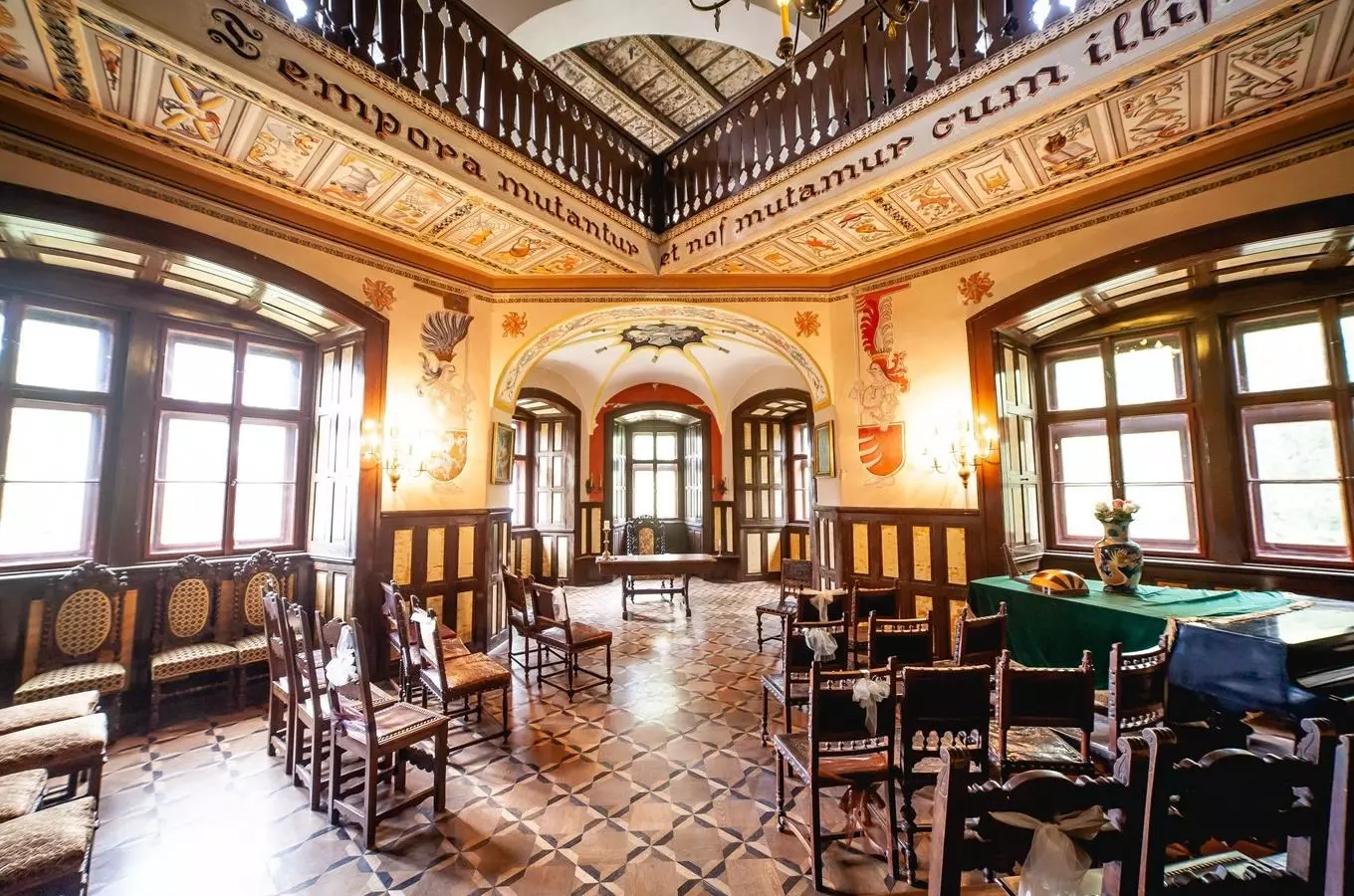 Vnitřní síň historického zámku s dřevěným mobiliárem a latinskými nápisy.