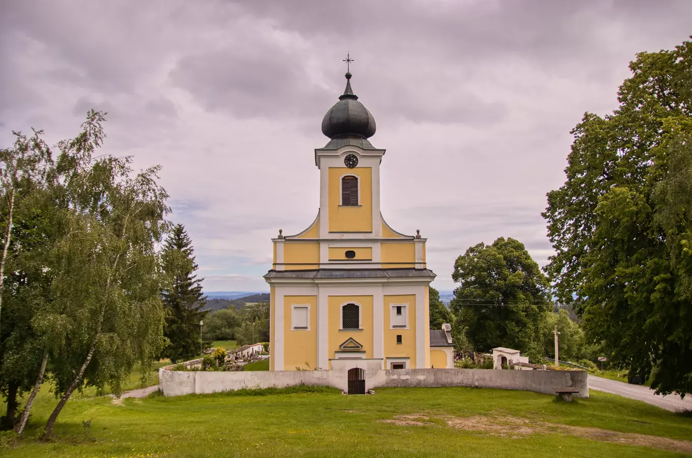 Žlutý kostel na kopci s hřbitovem v přírodě.