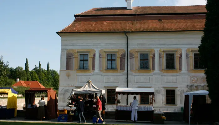Zámek Kratochvíle v Netolicích s tržními stánky před budovou.