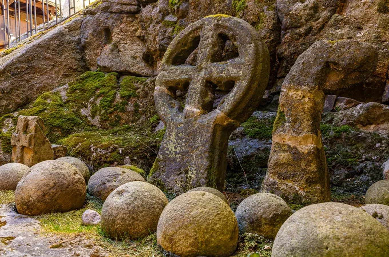Starověký keltský kříž z kamene mezi balvany u skalní stěny.
