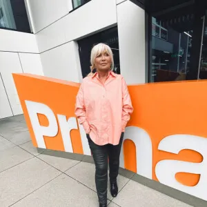 Žena stojí před oranžovou reklamní tabulí s logem Prima.