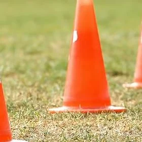 Oranžové dopravní kužely na trávníku pro sportovní cvičení.