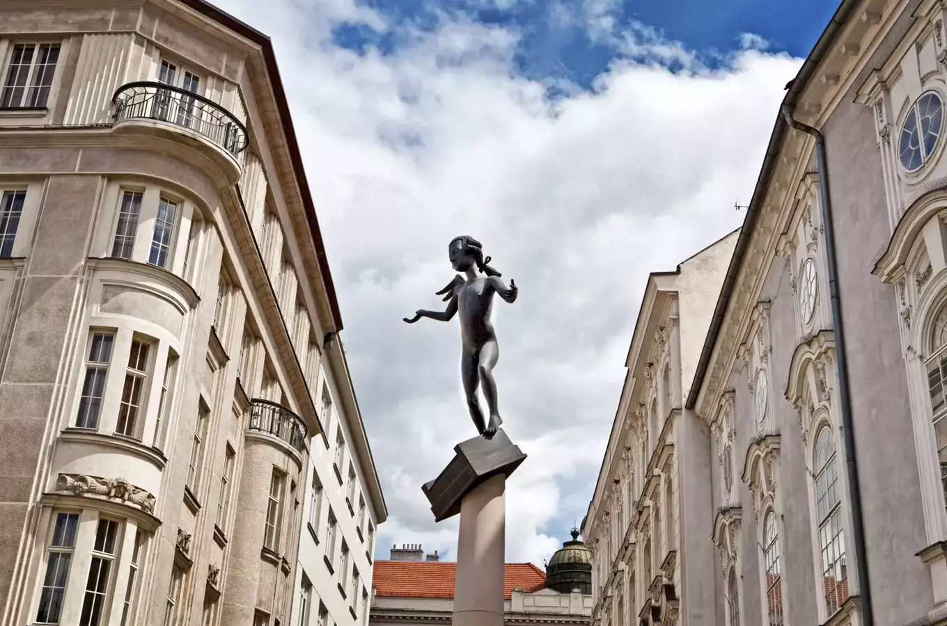 Socha dítěte na sloupu mezi dvěma historickými budovami v Brně.