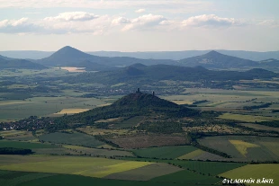 Pohled na kopcovitou krajinu s hradem v pozadí.