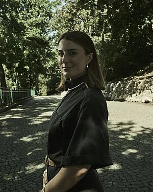 Žena v černém tričku stojí na kamenné cestě mezi stromy.