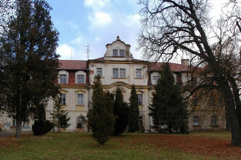 Historický zámek v Křimicích obklopený stromy.