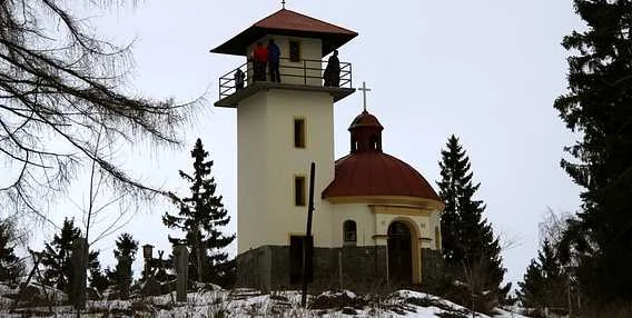 Bílá kostel s věží na sněhové hoře mezi stromy.