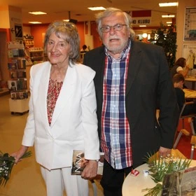 Dva seniorové stojí vedle sebe v knihkupectví s knihami.