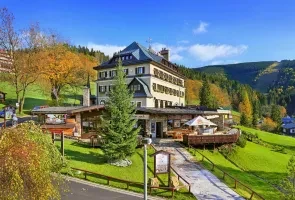Velký horský hotel v podhůří s lesy na pozadí.