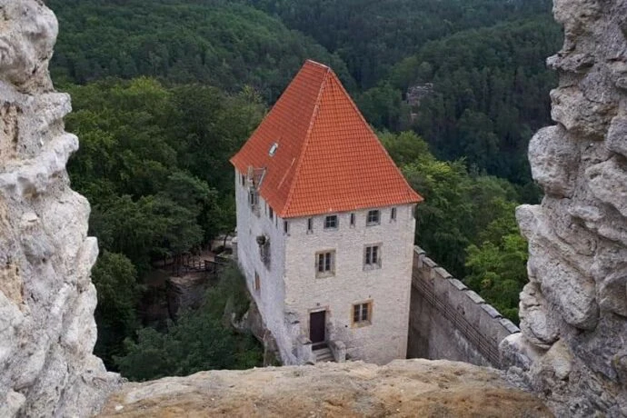 Zámek s červenou střechou na skále nad lesním údolím.
